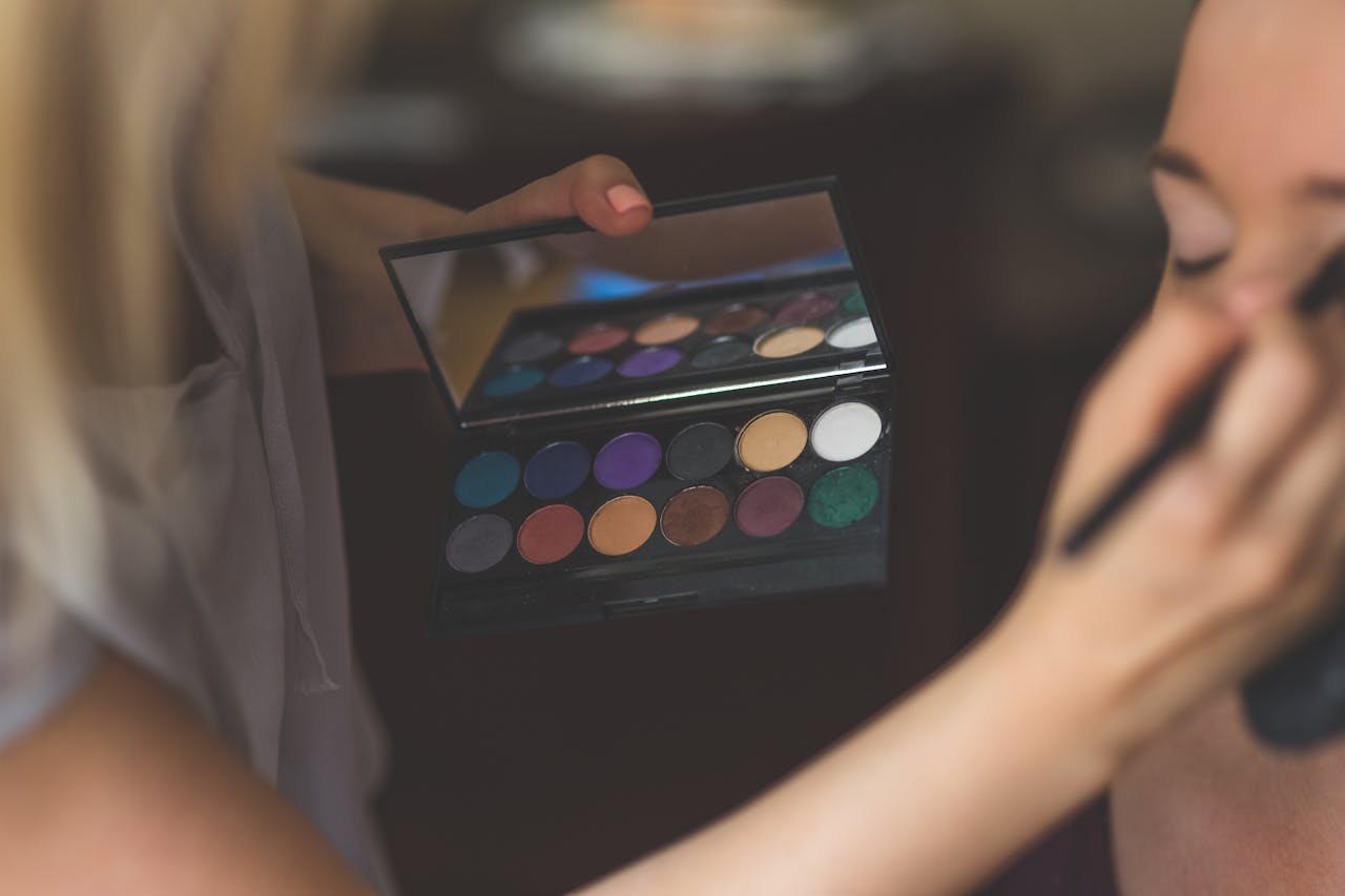 The Art of Drawing Readers In: Your attractive post title goes here A close-up of a stylist applying eyeshadow from a vibrant color palette to a model's face indoors.